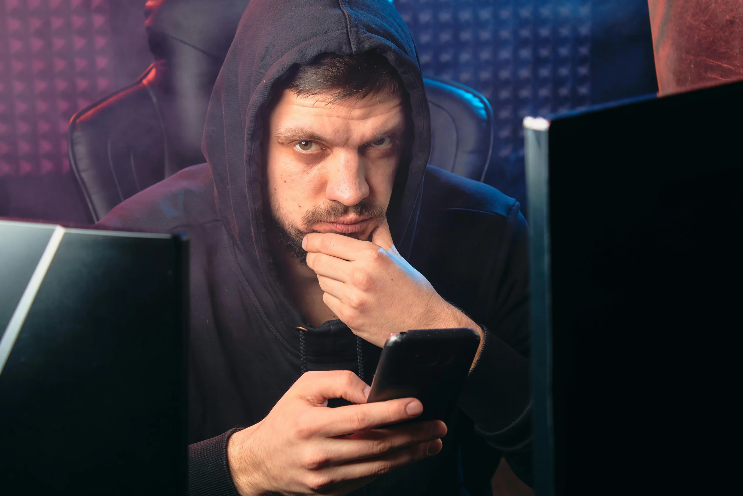 FAFSA refund — A man in a black hoodie contemplating while using a smartphone, surrounded by digital screens.