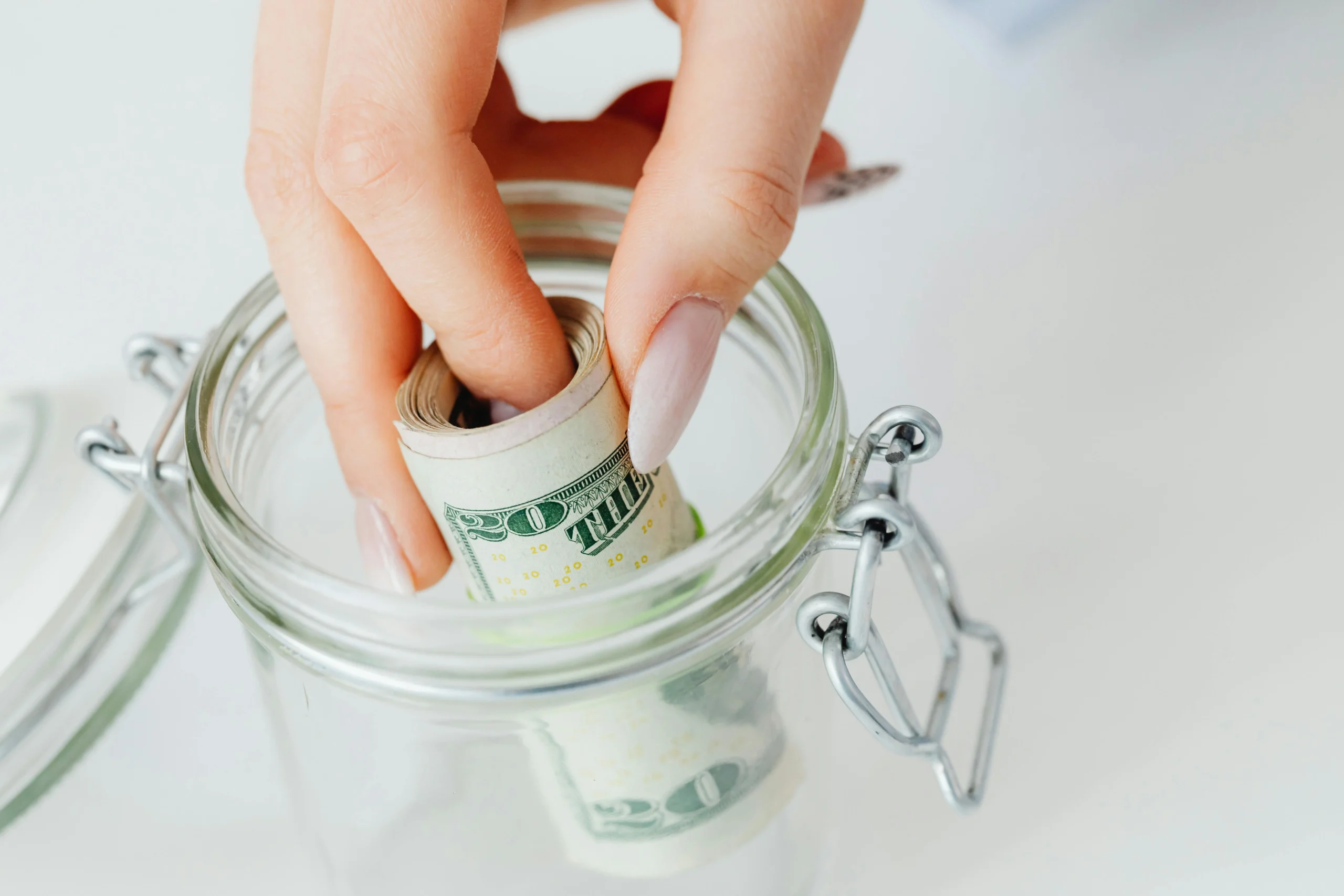family financial planning — A close-up of a hand placing rolled dollars into a glass jar, symbolizing savings.