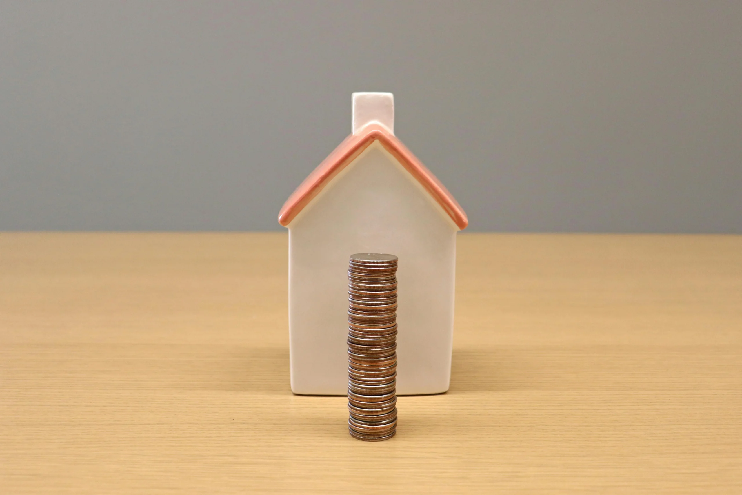 first time homebuyer programs 2026: A conceptual still life image of stacked coins in front of a porcelain house, symbolizing