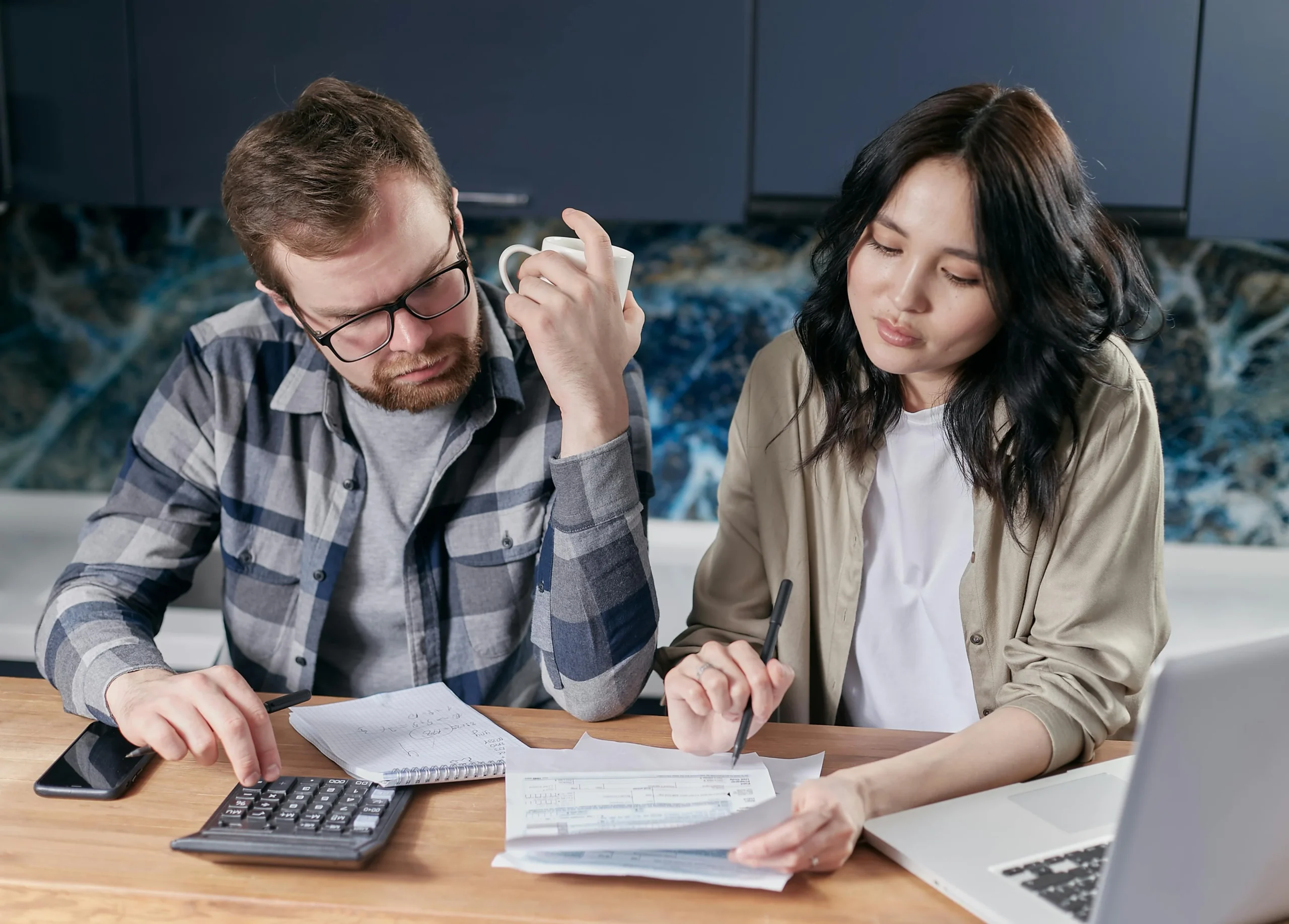 529 to Roth IRA rollover 2026: A couple reviewing household bills and budget using a calculator and laptop at their kitchen t