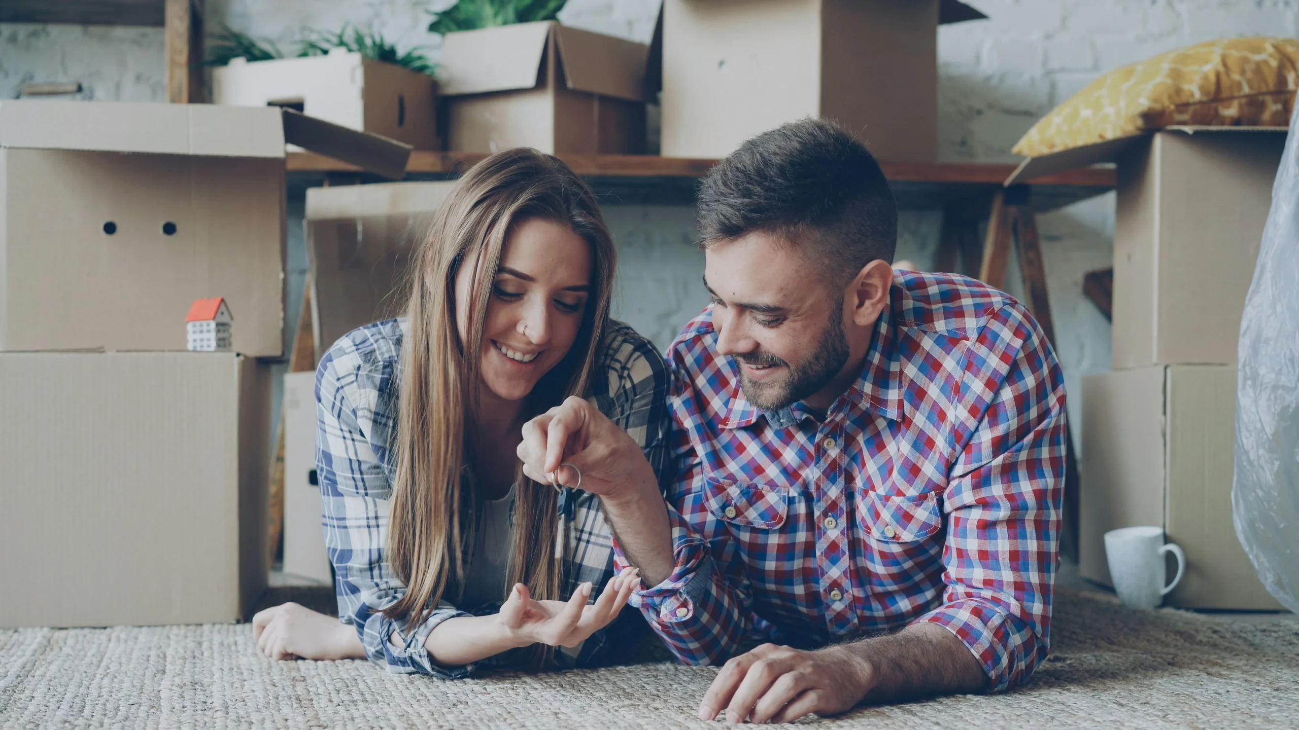 first time homebuyer programs 2026: Joyful couple laying on floor surrounded by moving boxes, holding keys to their new home