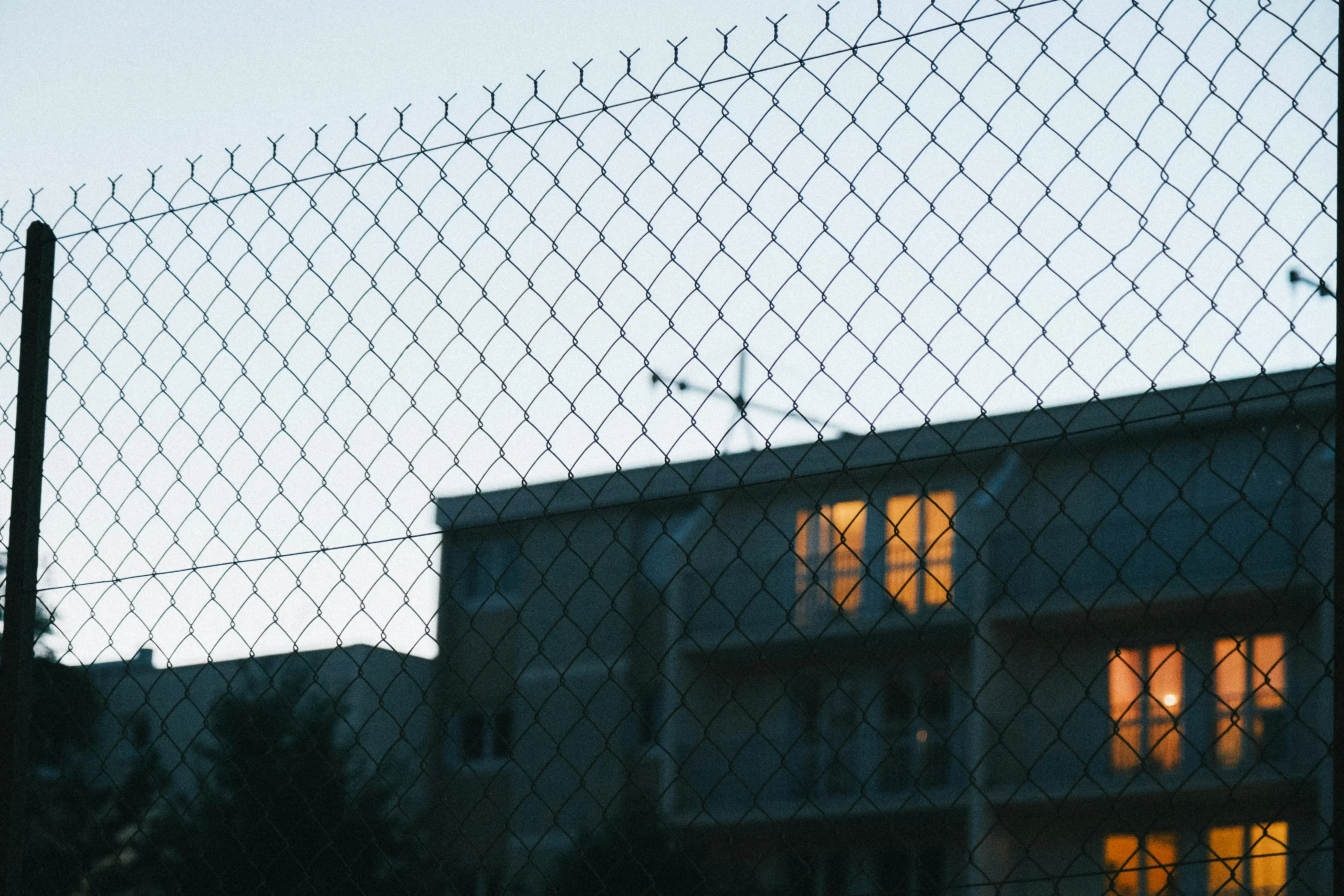 Homeowners Insurance Deductible Strategy 2026: 7 Proven Tips 1 homeowners insurance deductible strategy 2026: A city building with glowing windows viewed through a wire mesh fence at dusk
