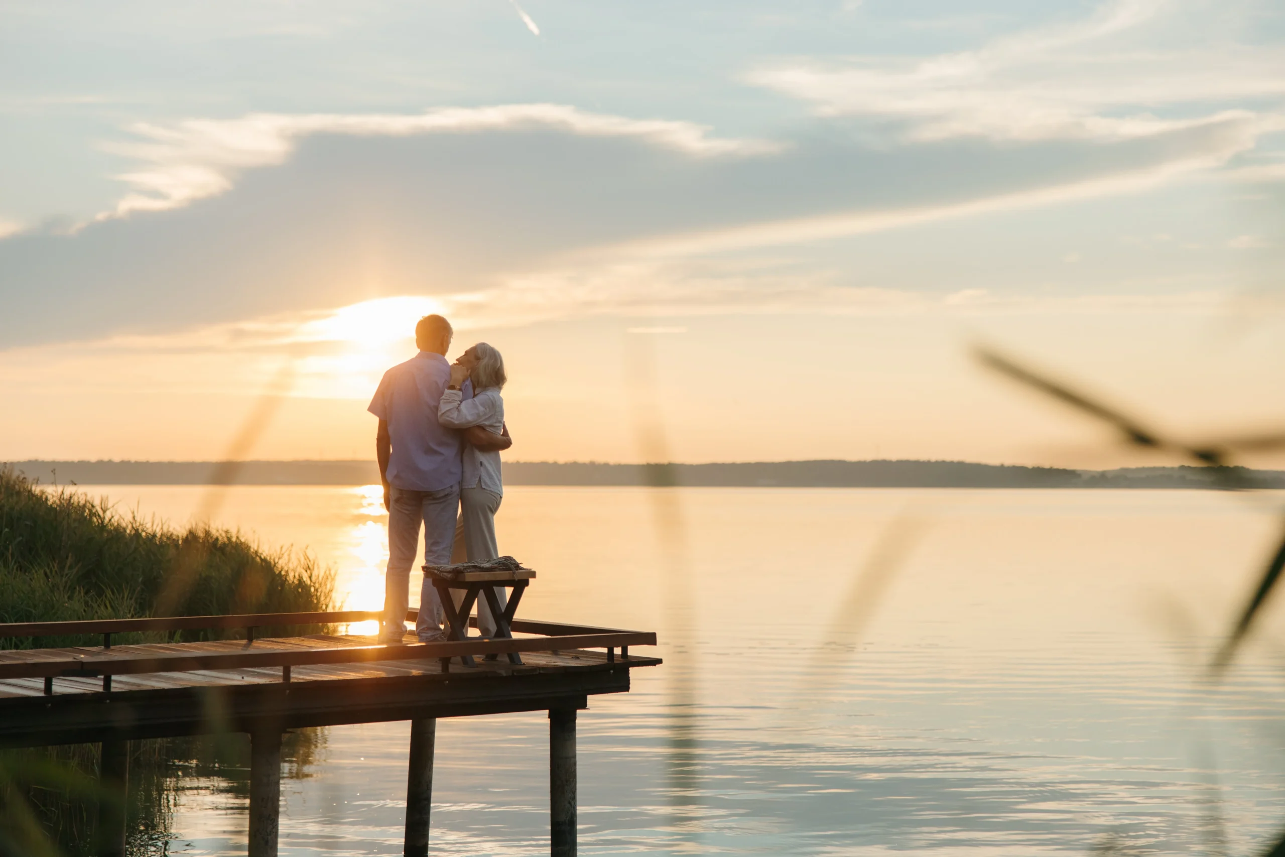 mega backdoor Roth 401k 2026: A senior couple embraces on a wooden dock at sunset, exuding tranquility and affection