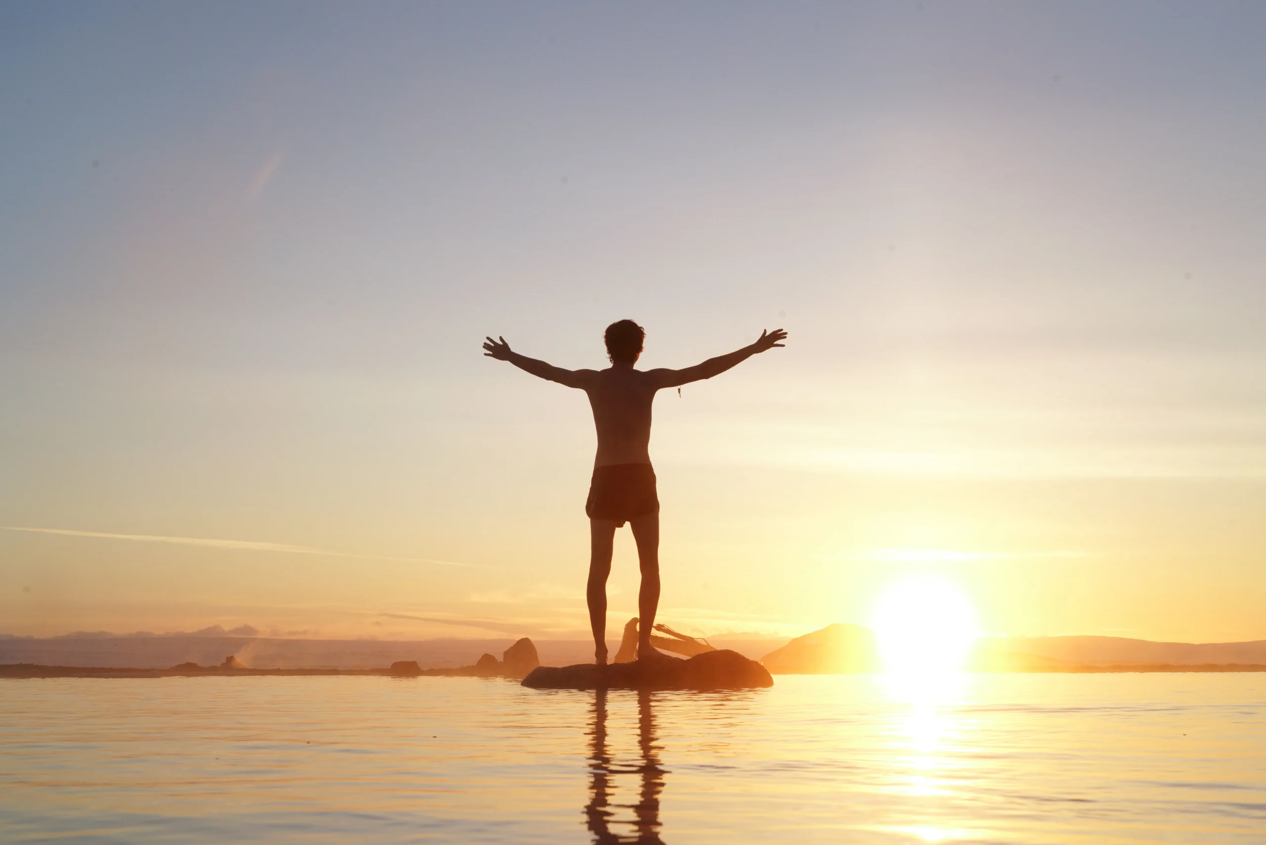 Roth conversion ladder 2026: Silhouette of a man standing on a rock with arms raised, facing the sunset over the ocean