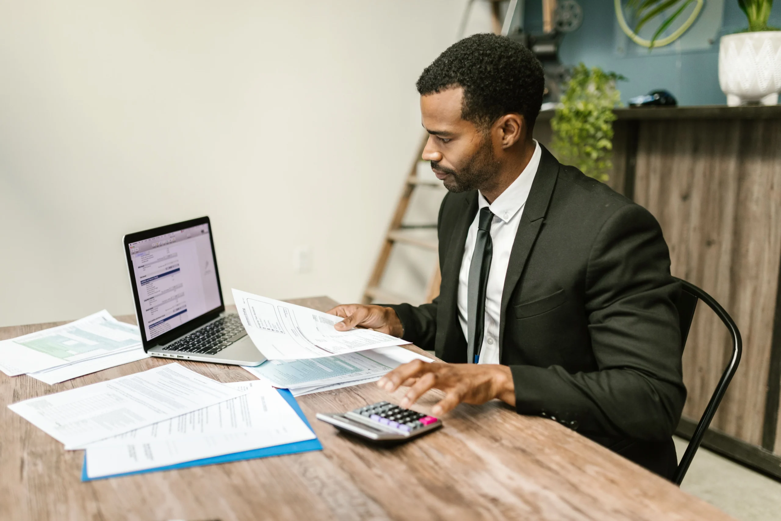 S corp salary vs distribution 2026: A businessman in a suit working on documents and using a laptop at an office desk