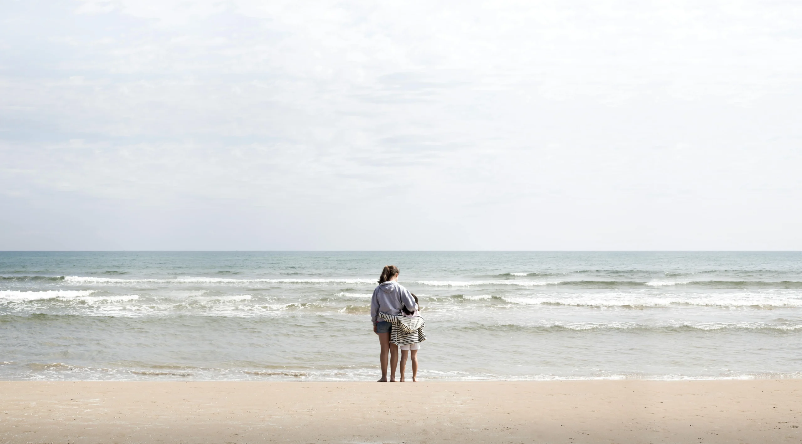 term vs whole life insurance 2026: A mother and child stand at the shoreline of a Valencia beach, gazing at the waves