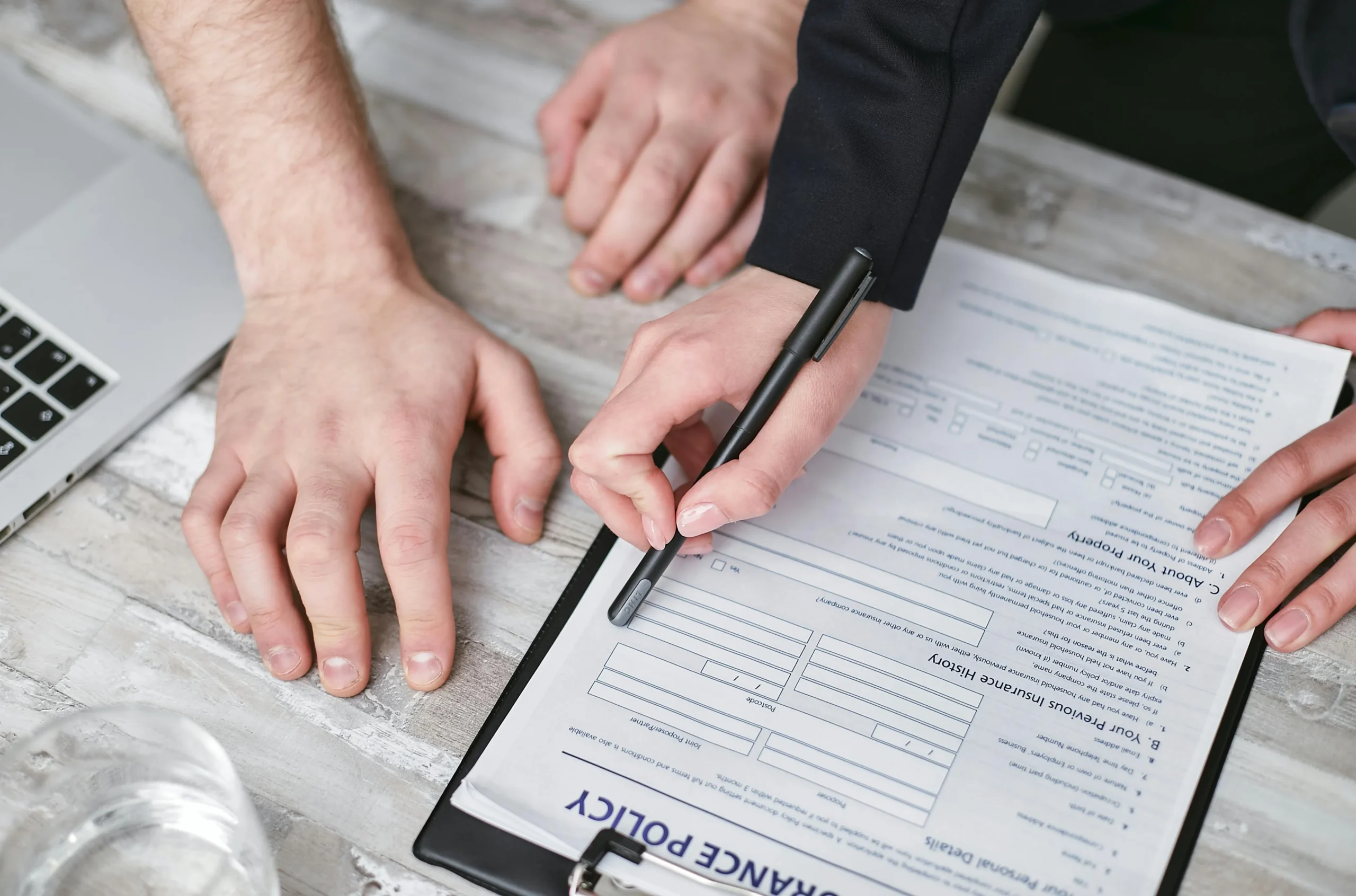 Pattern Day Trading Rule — Close-up image of two people signing an insurance policy document on a wooden desk.