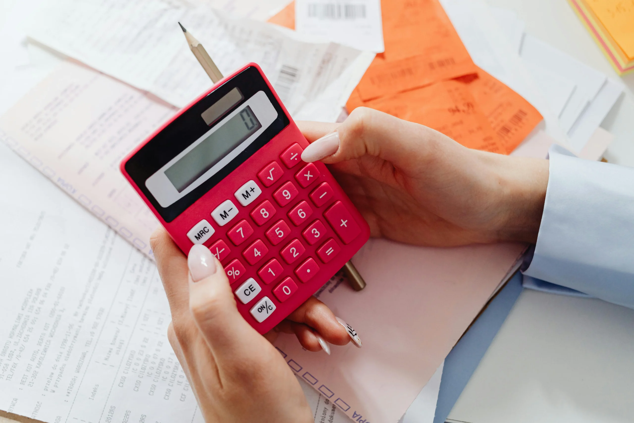 S corp salary vs distribution 2026: Close-up of hands holding a red calculator, managing finances with documents and receipts