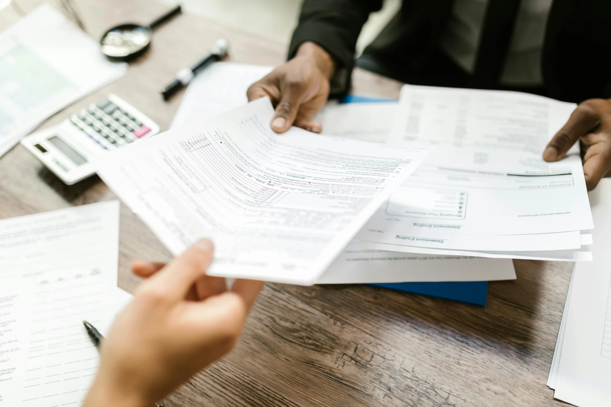 S corp salary vs distribution 2026: Two professionals exchanging documents in an office setting, focusing on paperwork and da