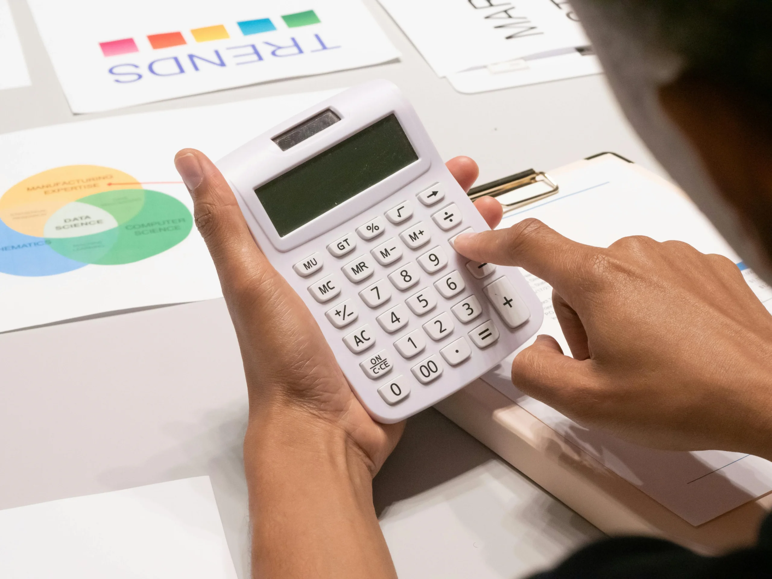 Student Aid Index — Close-up of a person's hand using a calculator on a desk with financial documents.