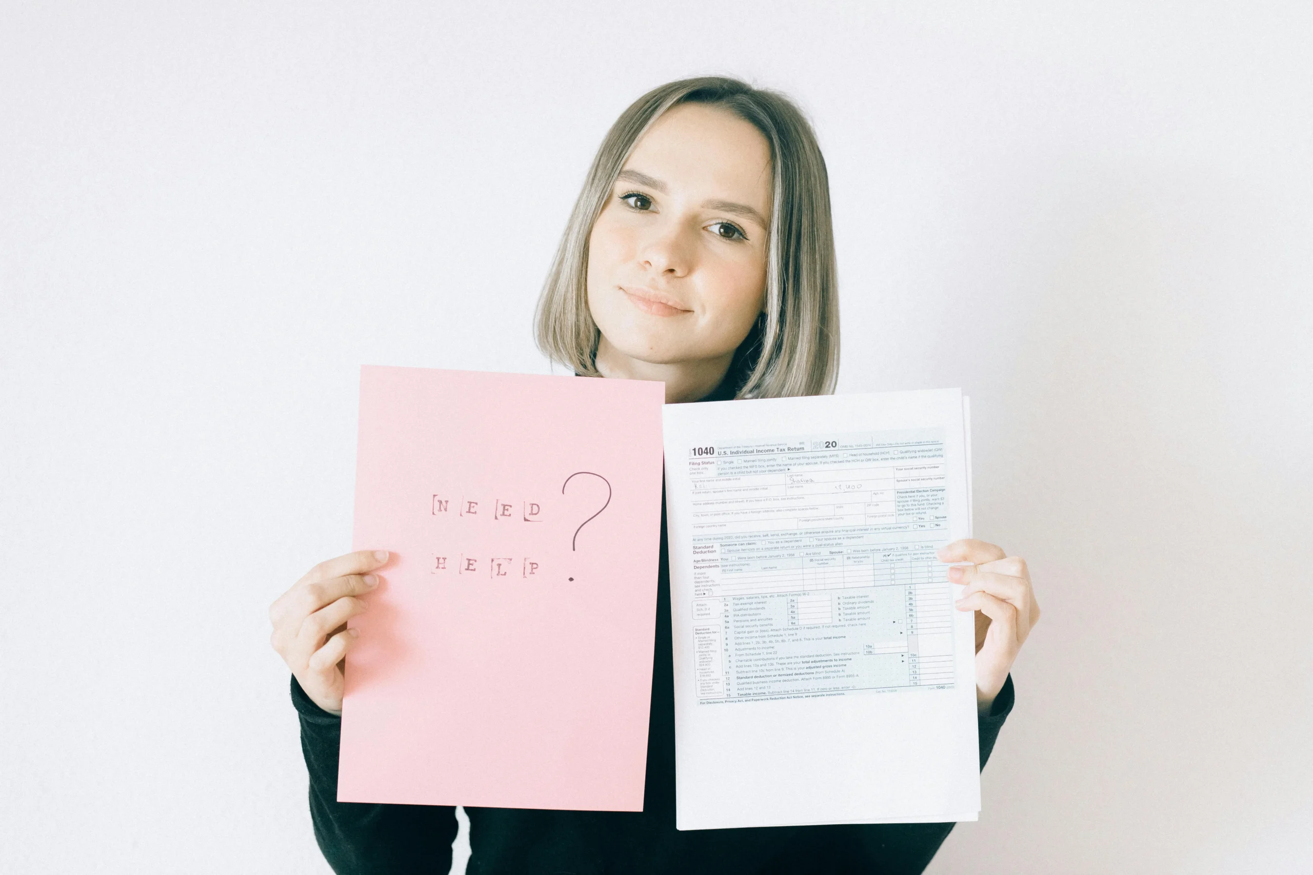 tax credits for families 2026: A woman in a black shirt holds tax forms and a 'Need Help?' sign, indoors