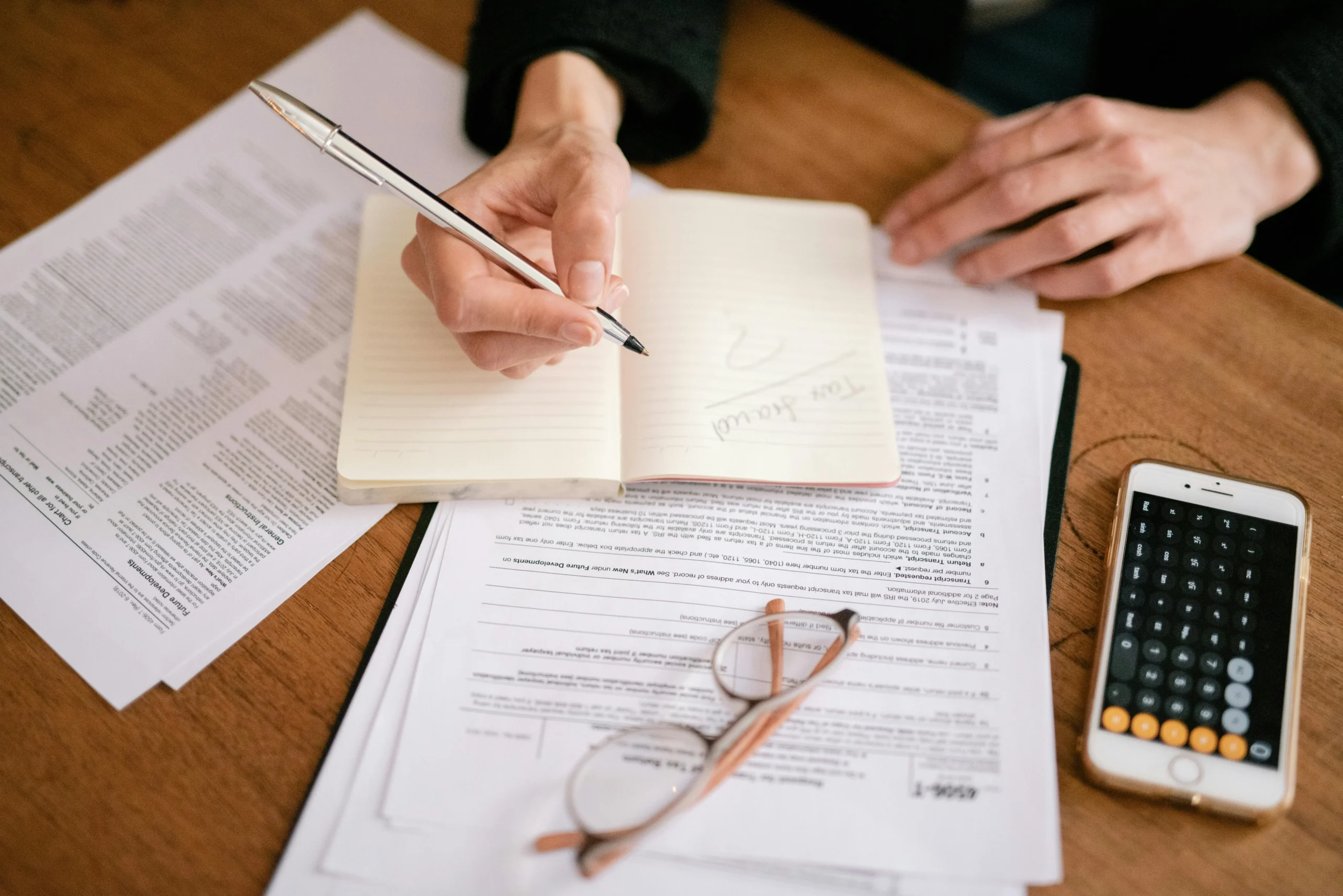 traditional vs Roth 401k 2026: Close-up of a person writing in a notebook with documents and a calculator, managing finances